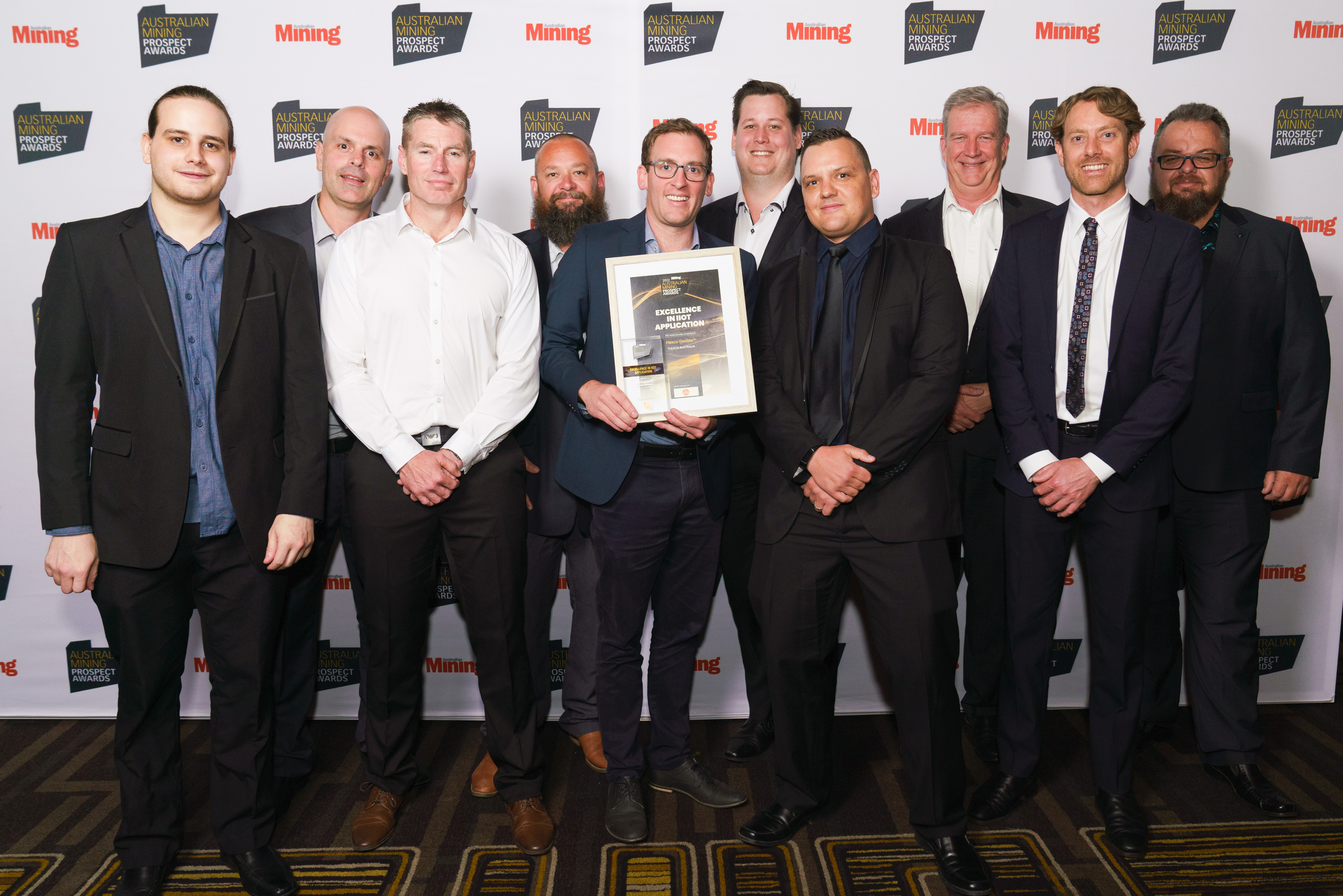 Ten men standing together and smiling.  The man in the center is holding a framed award.